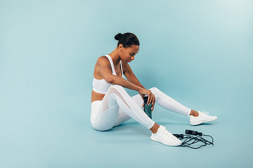 Tired woman sitting on blue background in studio after training