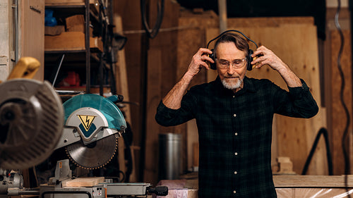 Senior carpenter wearing noise-canceling headphones preparing for working on saw machine