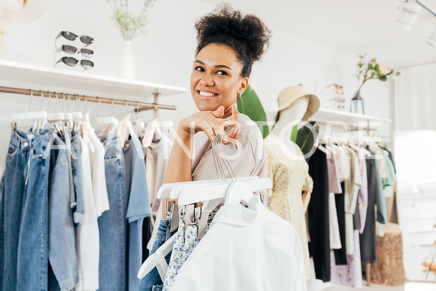 Smiling saleswoman working in boutique holding a bunch of hangers with clothes