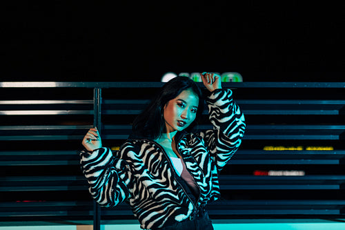 Young woman posing on a roof in front of a city lights and looking at camera