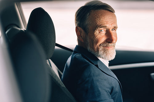 Side view of a senior driver looking away. Man in formal wear sitting inside a car.