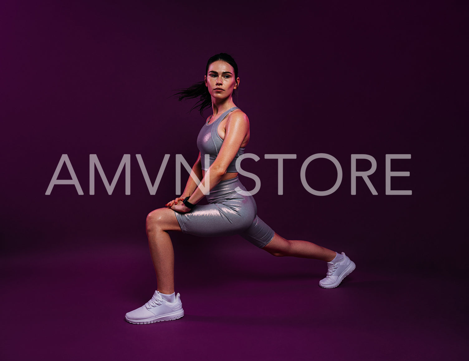 Slim female in silver fitness attire warming up her body against a magenta background