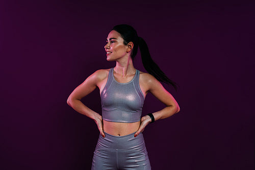 Confident female athlete with hands on hips looking away standing against a magenta background