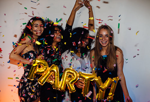 Group of young women celebrating with confetti, standing indoors