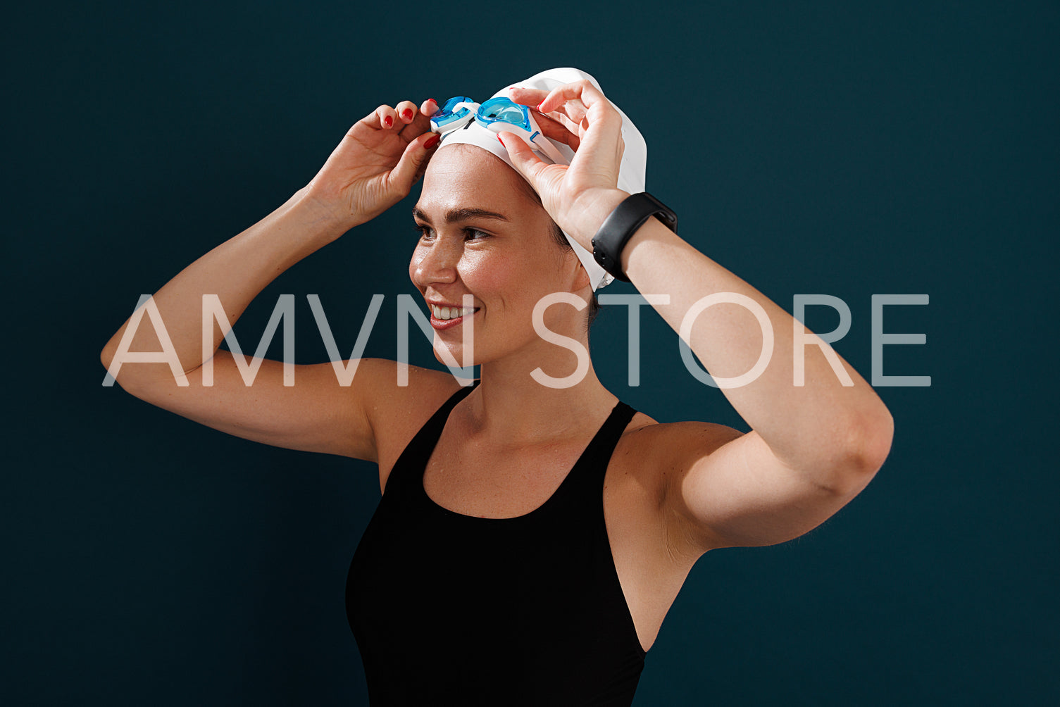 Portrait of a young female swimmer wearing goggles standing against a blue backdrop