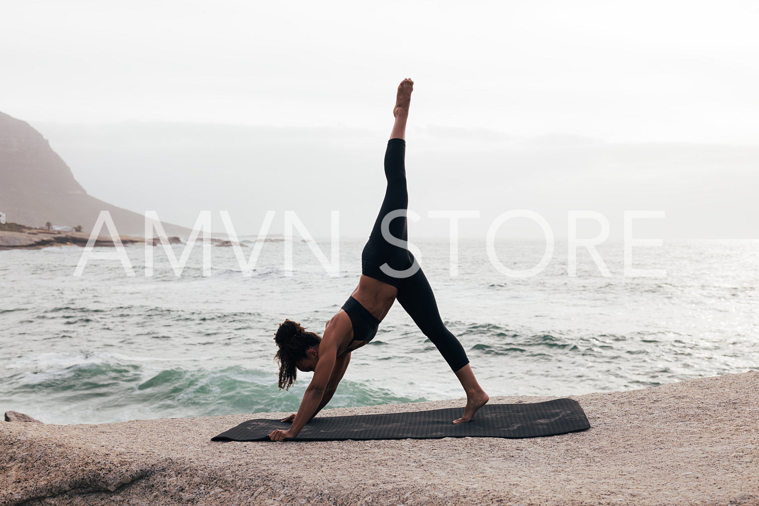 Side view of young woman doing Three-Legged Down Dog pose by ocean at sunset