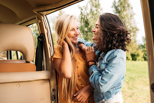 Two young women friends standing at camper van looking at each other