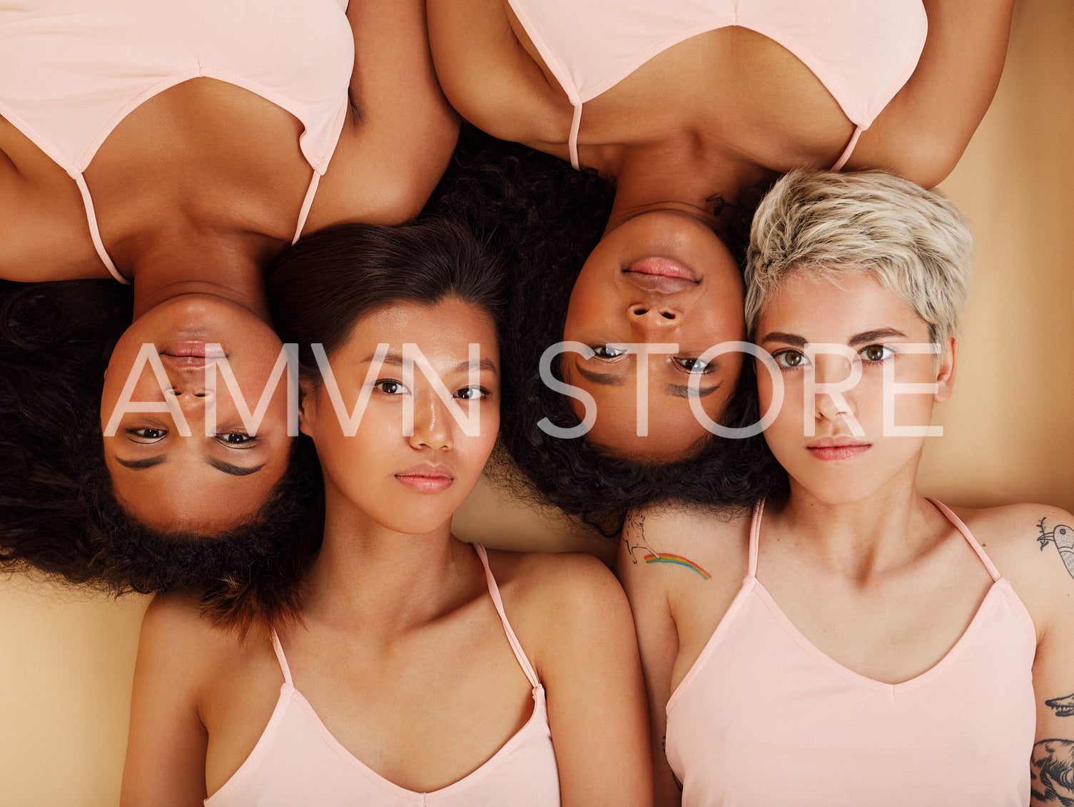 Group of four women lying together in a studio and looking at the camera. Diverse females lying head to head.