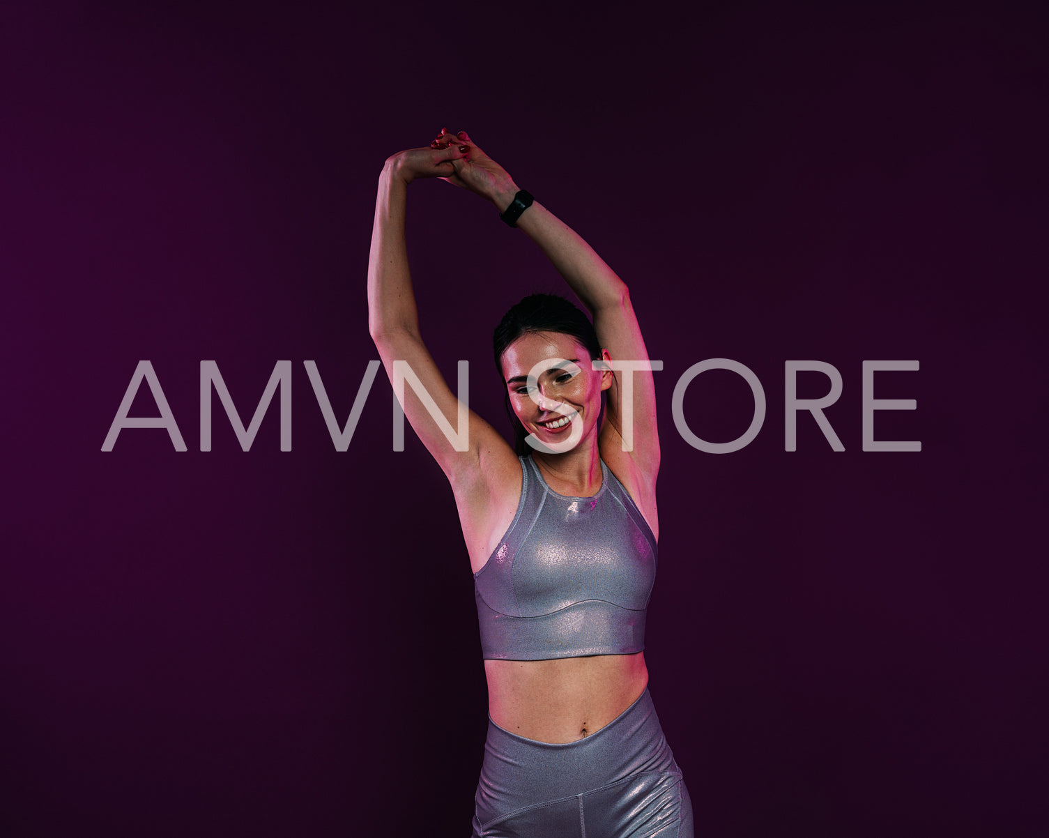 Positive woman in silver sportswear flexing her hands on a magenta background