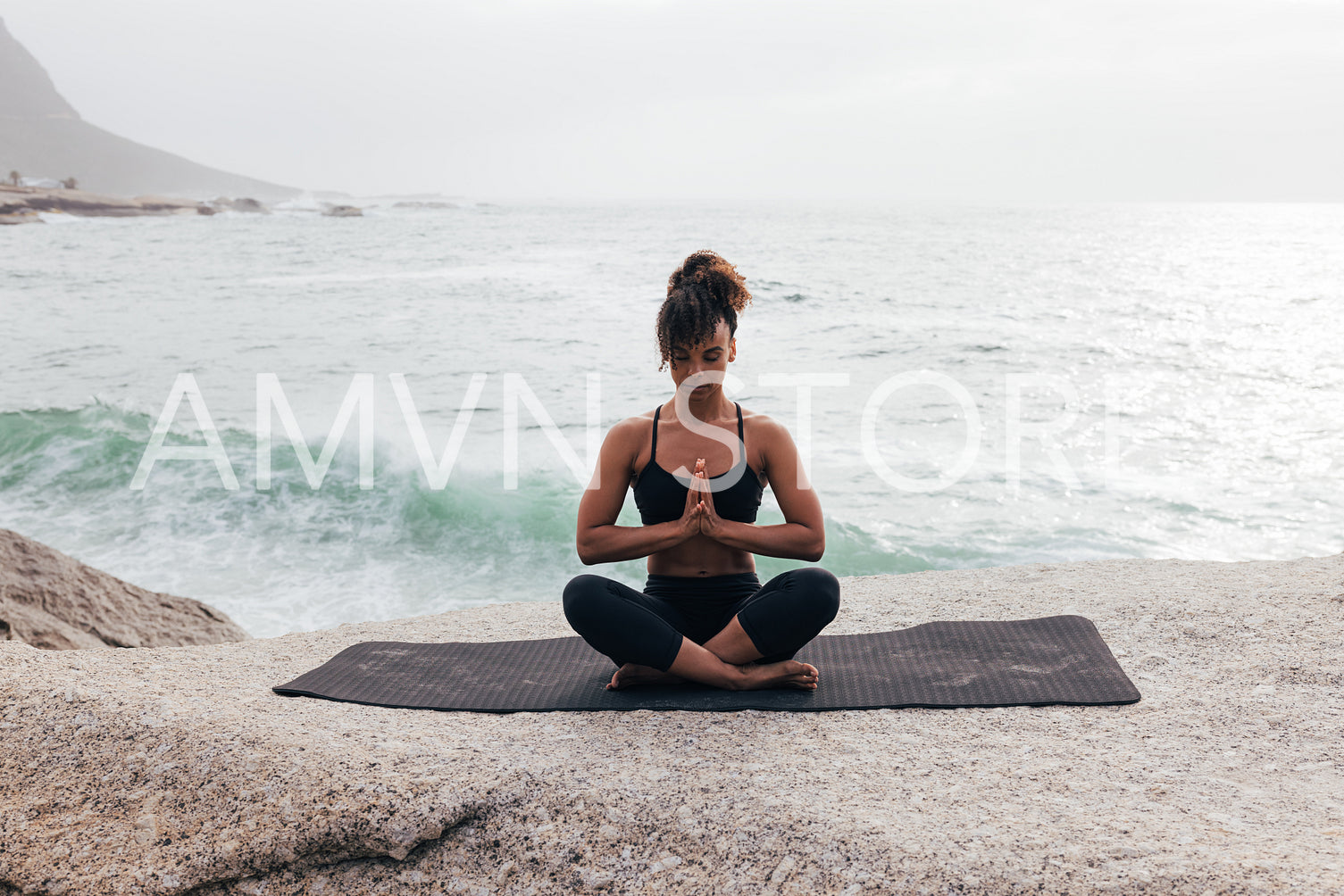 Fit woman with crossed legs meditating while sitting on mat by ocean