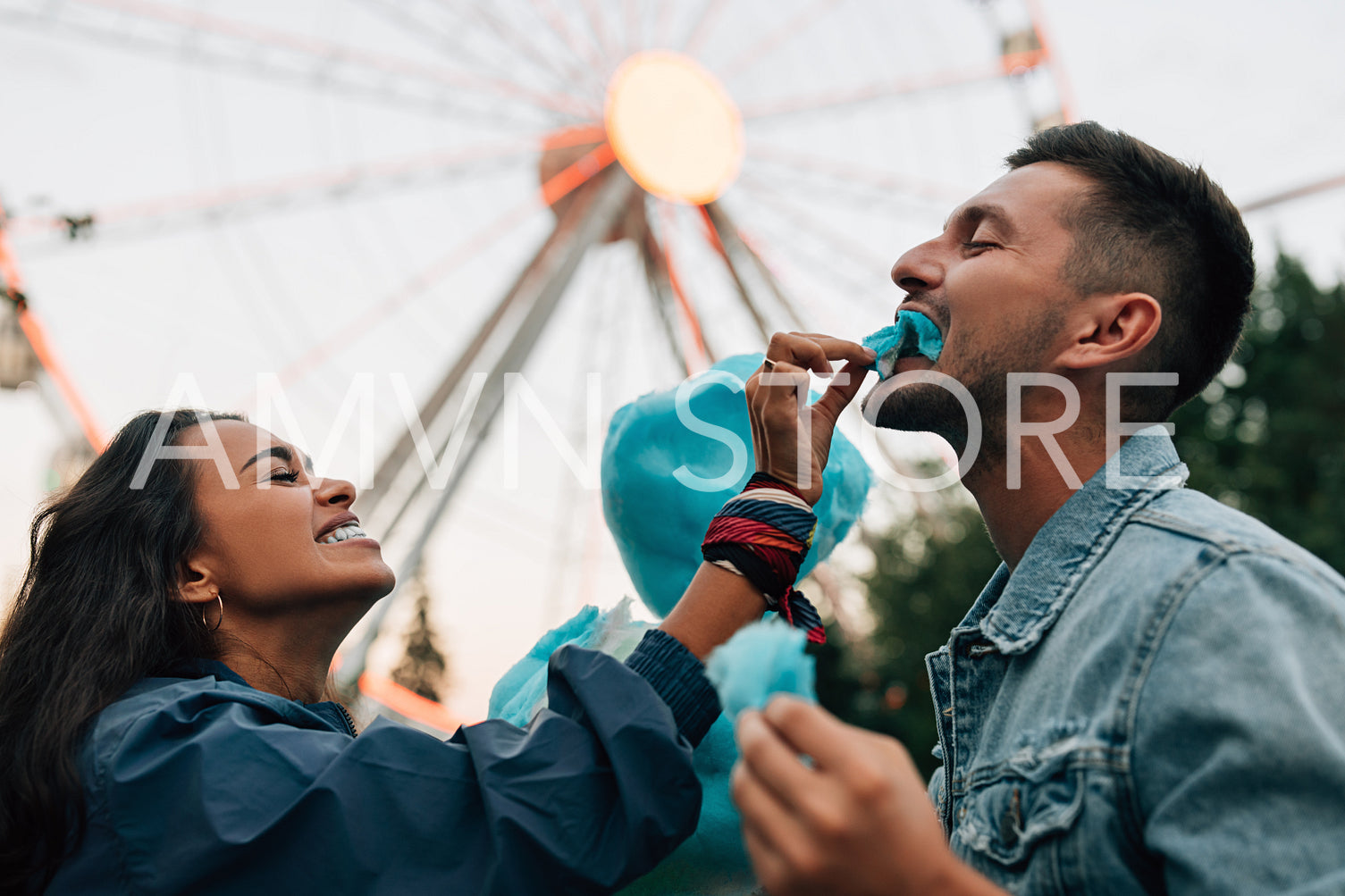 Laughing girlfriend feeding her boyfriend with cotton candy. Young couple having fun in amusement park eat cotton candy.