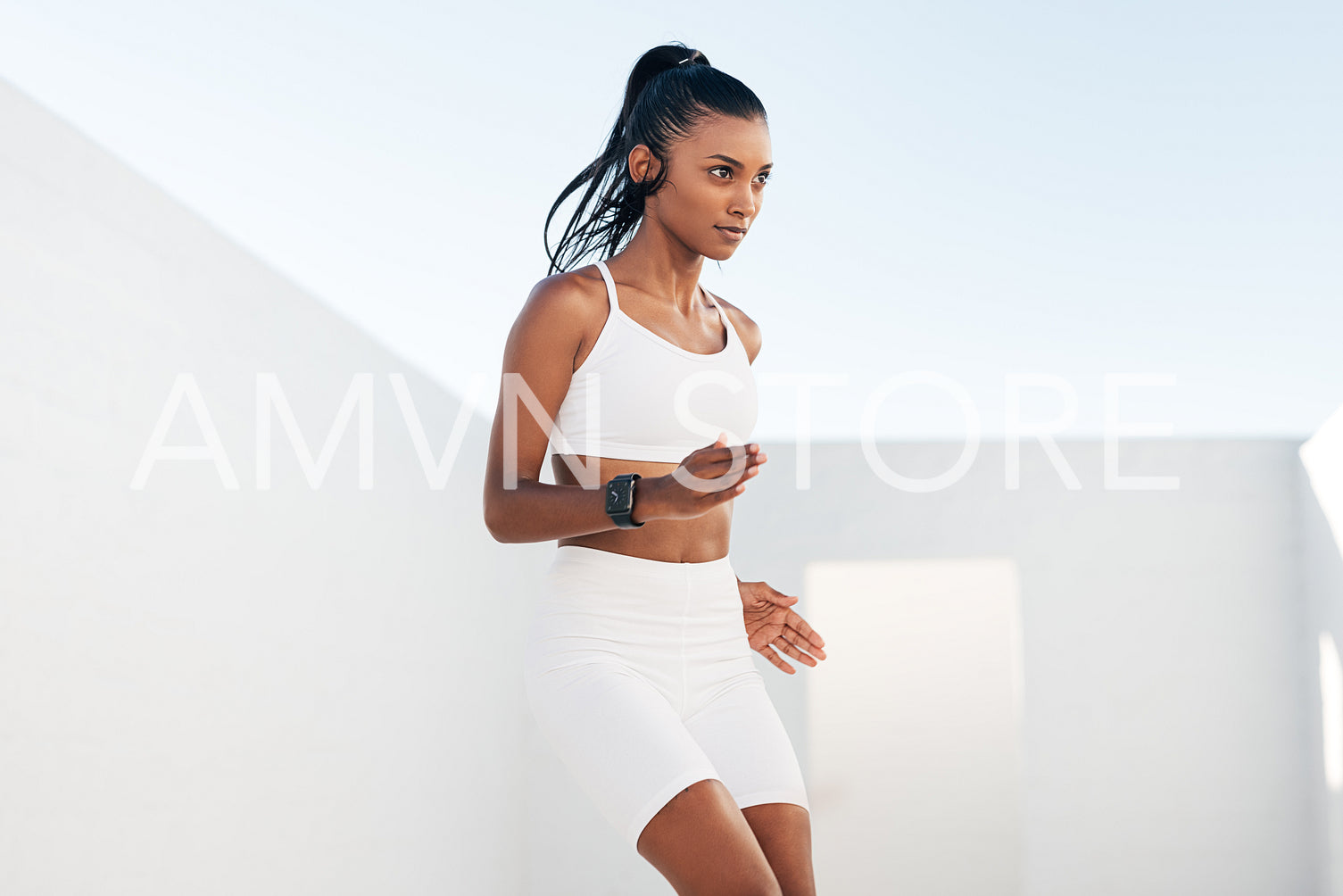 Slim woman in white fitness attire warming up outdoors. Young female jumping up and down.