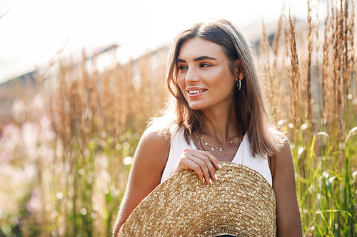 Smiling woman standing outdoors with big straw hat surrounded by tall grass