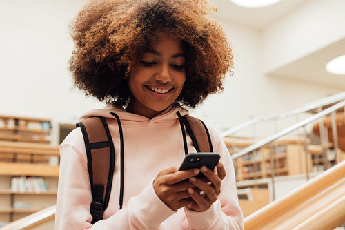 Smiling girl holding smartphone in high school library