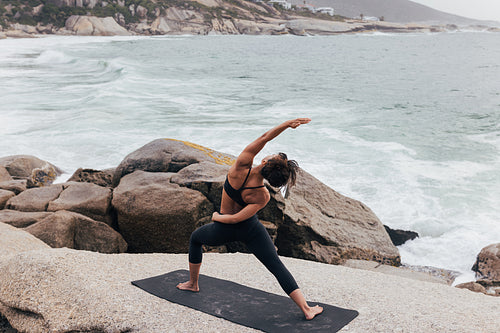 Healthy female practicing Utthita Parsvakonasana yoga pose. Woman exercising near an ocean.