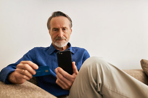 Senior man paying online. Male in casual clothes sitting on sofa holding a credit card