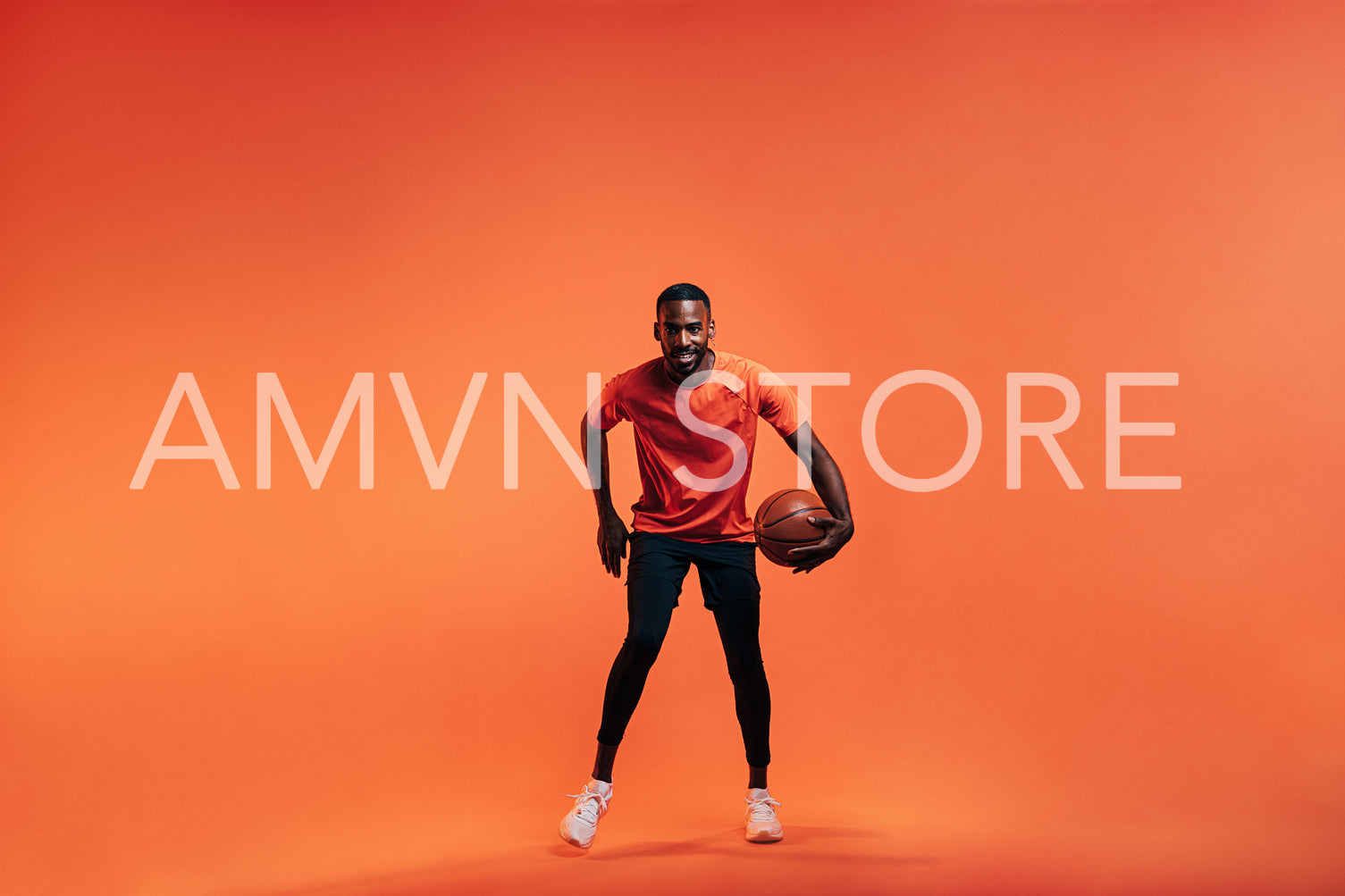 Young sportsman dribbling basket ball in studio against an orange background