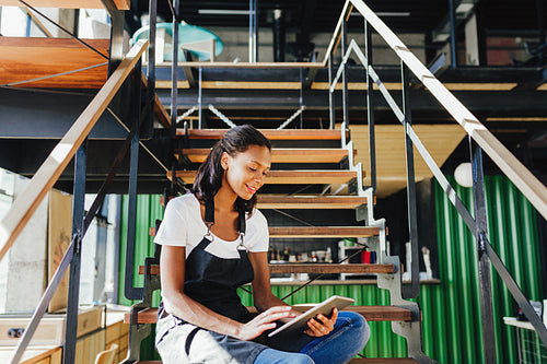 Coffee shop owner sitting on staircase and reviewing business files on digital tablet