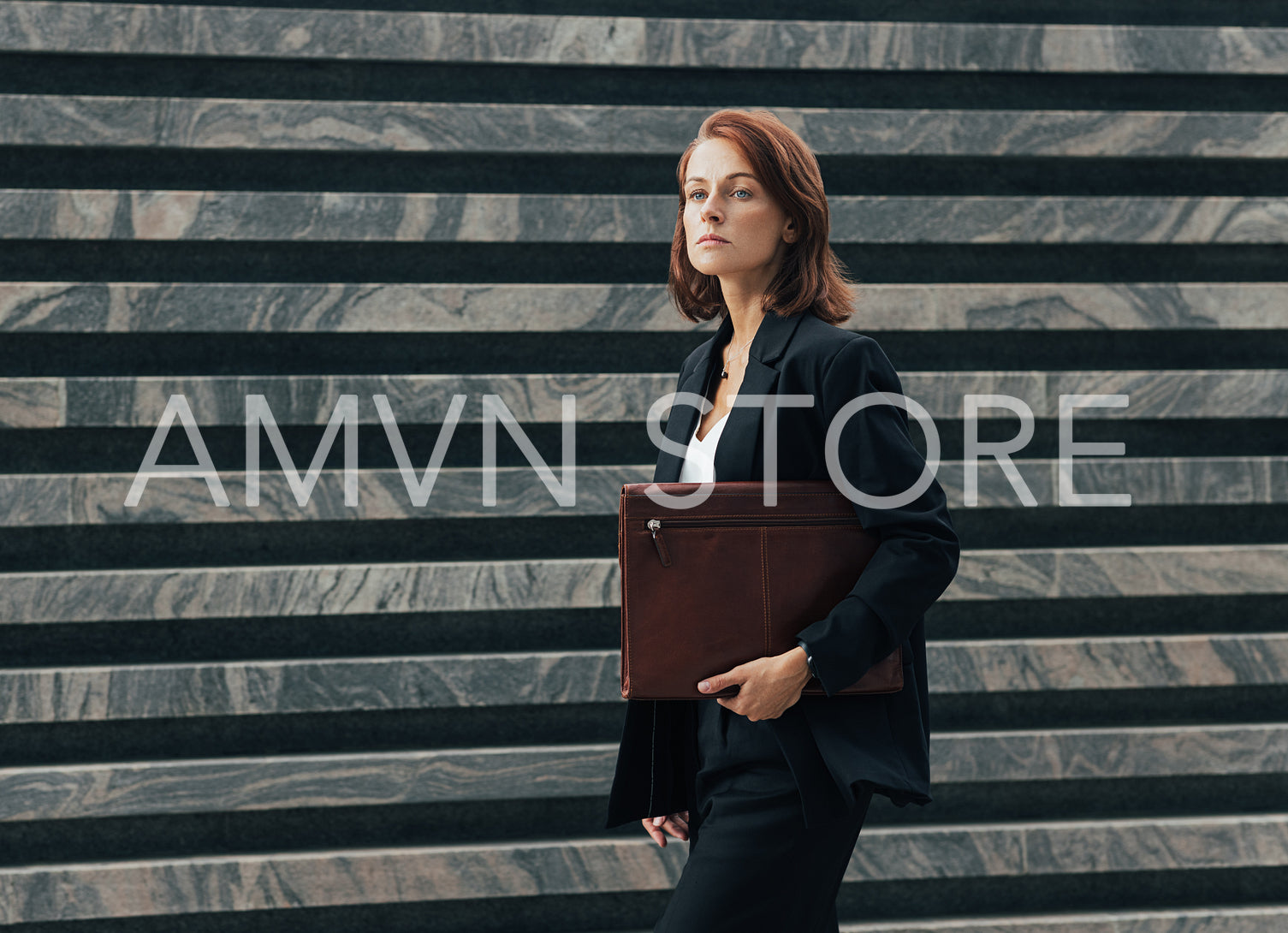 Confident middle-aged female in formal black clothes walks outdoors with a leather folder. Female with ginger hair is going to a corporate meeting.