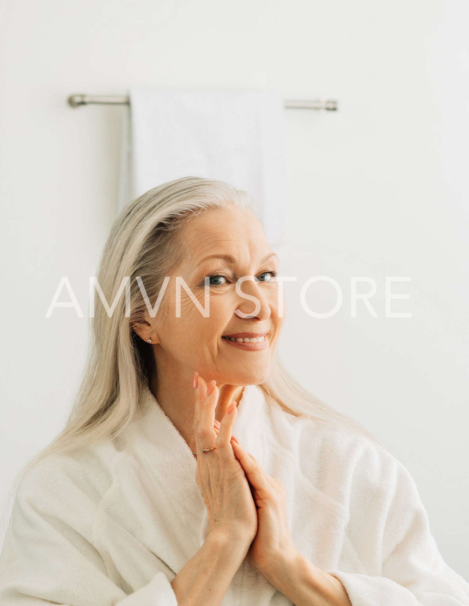 Smiling female with grey hair admires her reflection while standing in front of a bathroom mirror in the morning