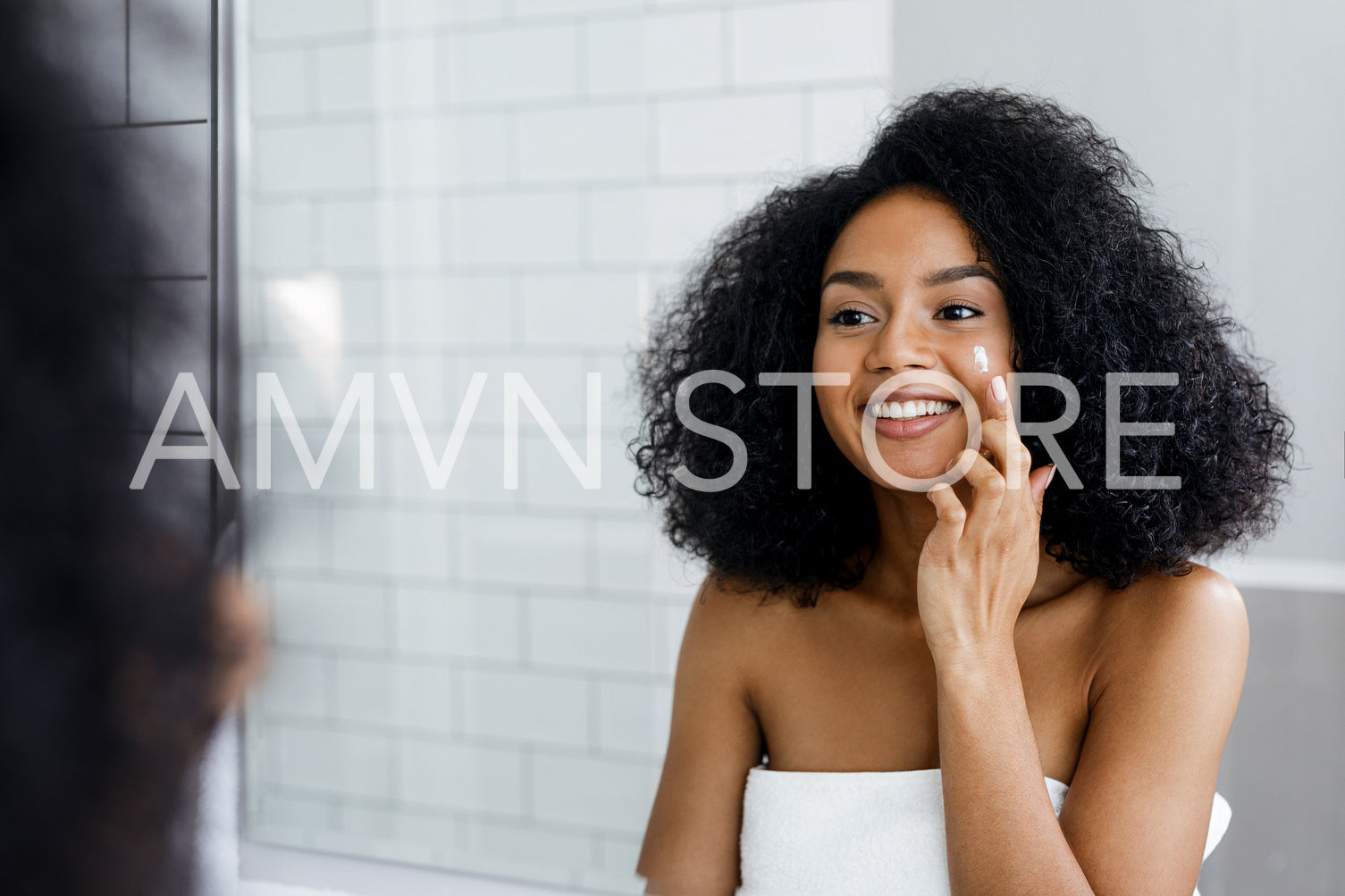 Happy young woman applying face cream with finger in bathroom	