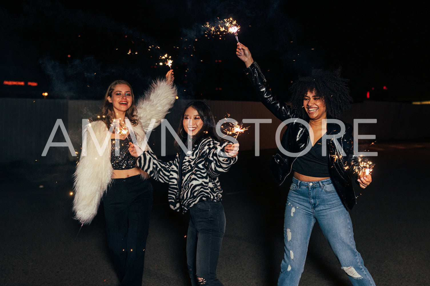 Three laughing female friends waving sparklers at night and having fun together	