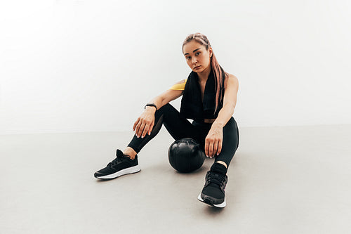 Woman in sports clothes and with black towel on her neck relaxing after exercises with a medicine ball