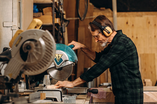 Side view of craftsperson using circular saw over wooden plank at workshop