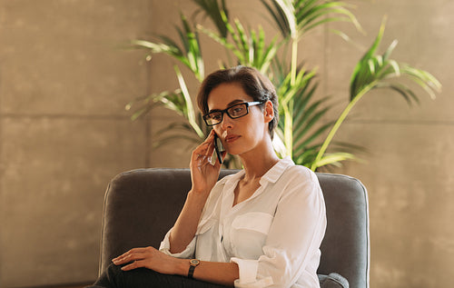 Middle-aged businesswoman in formal wear talking on mobile phone while sitting indoors