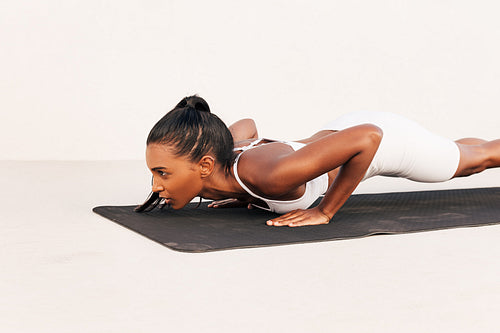 Side view of a slim sportswoman making push-ups on a black mat outdoors