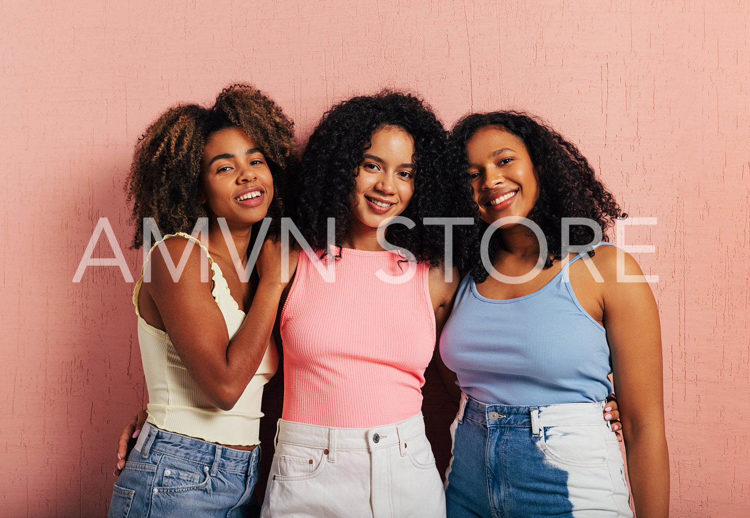 Three beautiful smiling women with curly hair standing together at pink wall