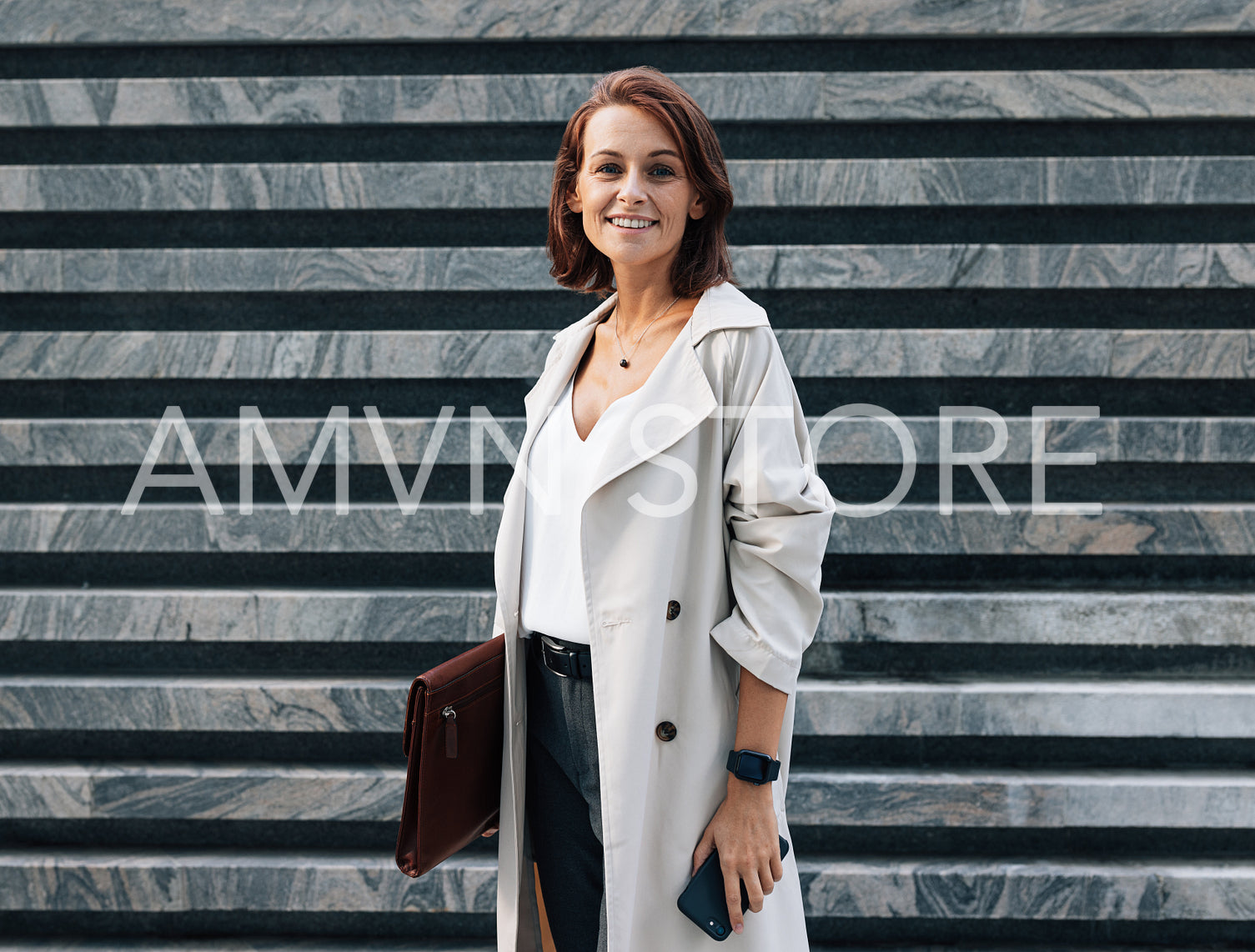 Cheerful middle-aged woman in stylish clothes looking at the camera while standing outdoors. Female in coat with leather folder. Woman with ginger hair wearing stylish clothes.