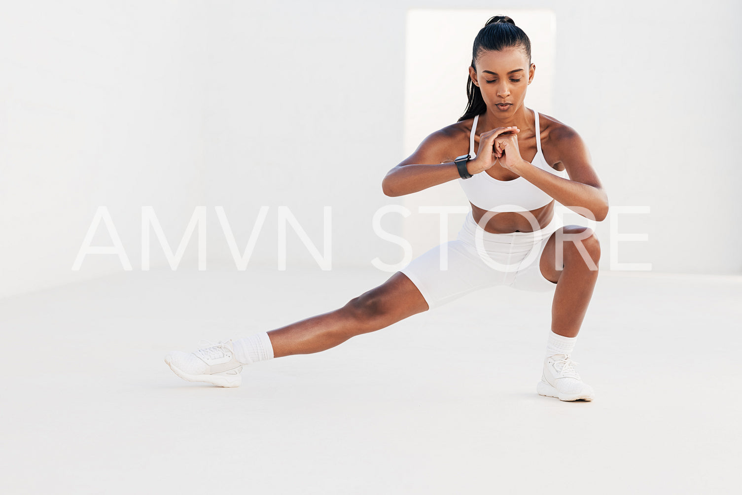 Woman with closed eyes stretching her leg. Slim female warming up her body in a white studio.