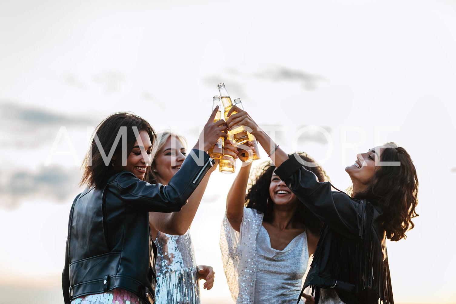 Four happy friends toasting with beer bottles at sunset	