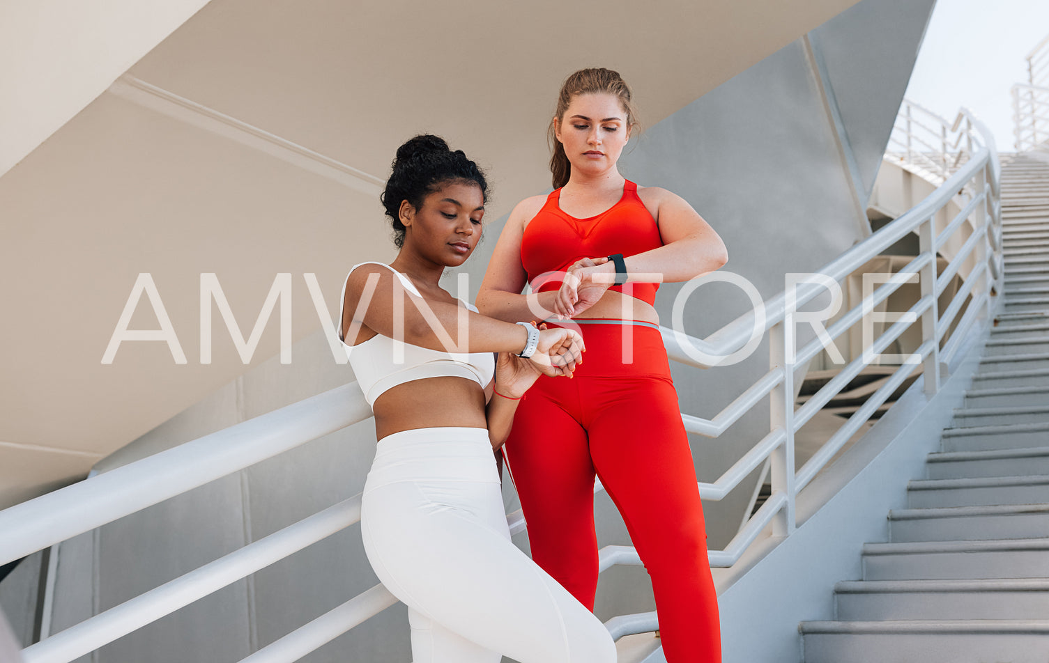 Two plus-size females standing together checking their smartwatches. Full-figured women in fitness attire relax after workout checking their pulse on smartwatches.