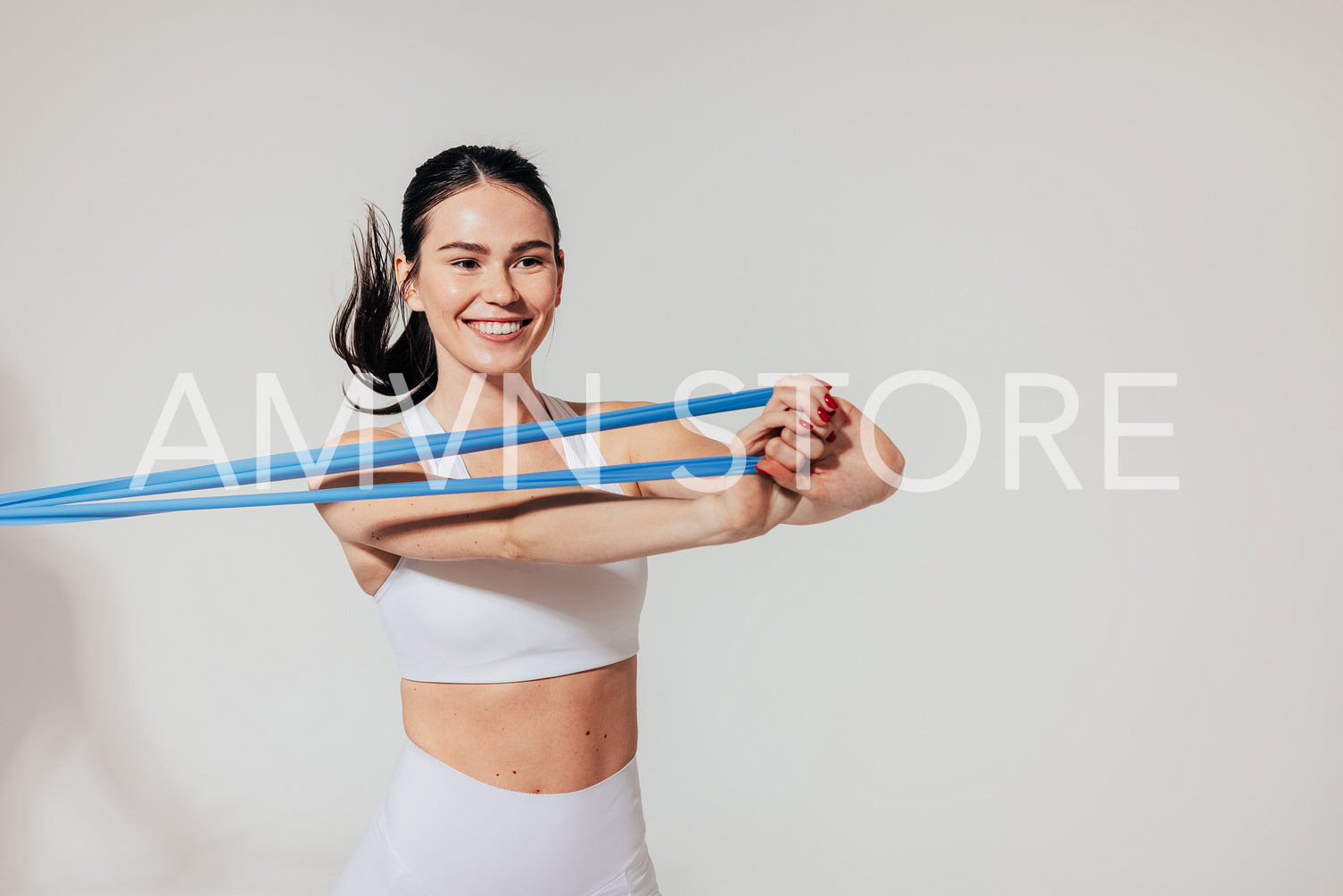 Happy sportswoman in white fitness wear pulling resistance band