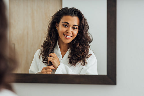 Reflection of a brunette woman in bathroom mirror touching hair