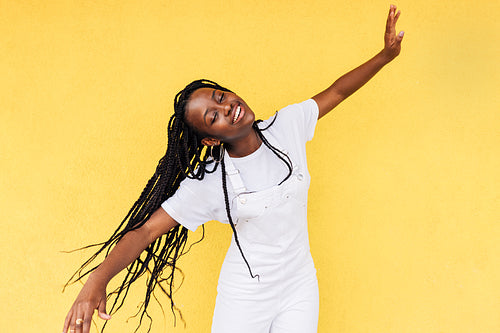 Smiling woman in white casual clothes having fun against a yellow wall outdoors