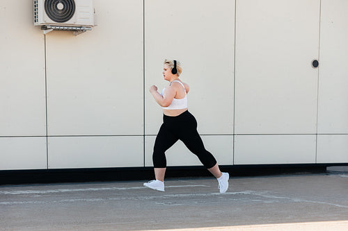 Side view of a woman with plus size body running at wall outdoors