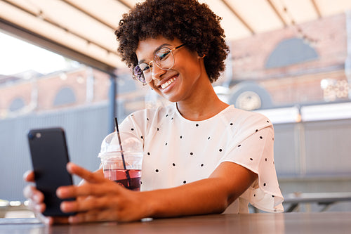 Happy girl posting new content in social media. Beautiful woman chatting from outdoor cafe.