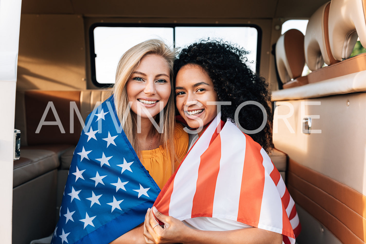 Cheerful female friends sitting together in a camper van with an American flag. Young women enjoying the 4th of July holiday.