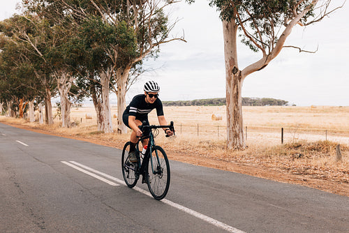 Woman cyclist sprinting on her bicycle while riding on empty country road