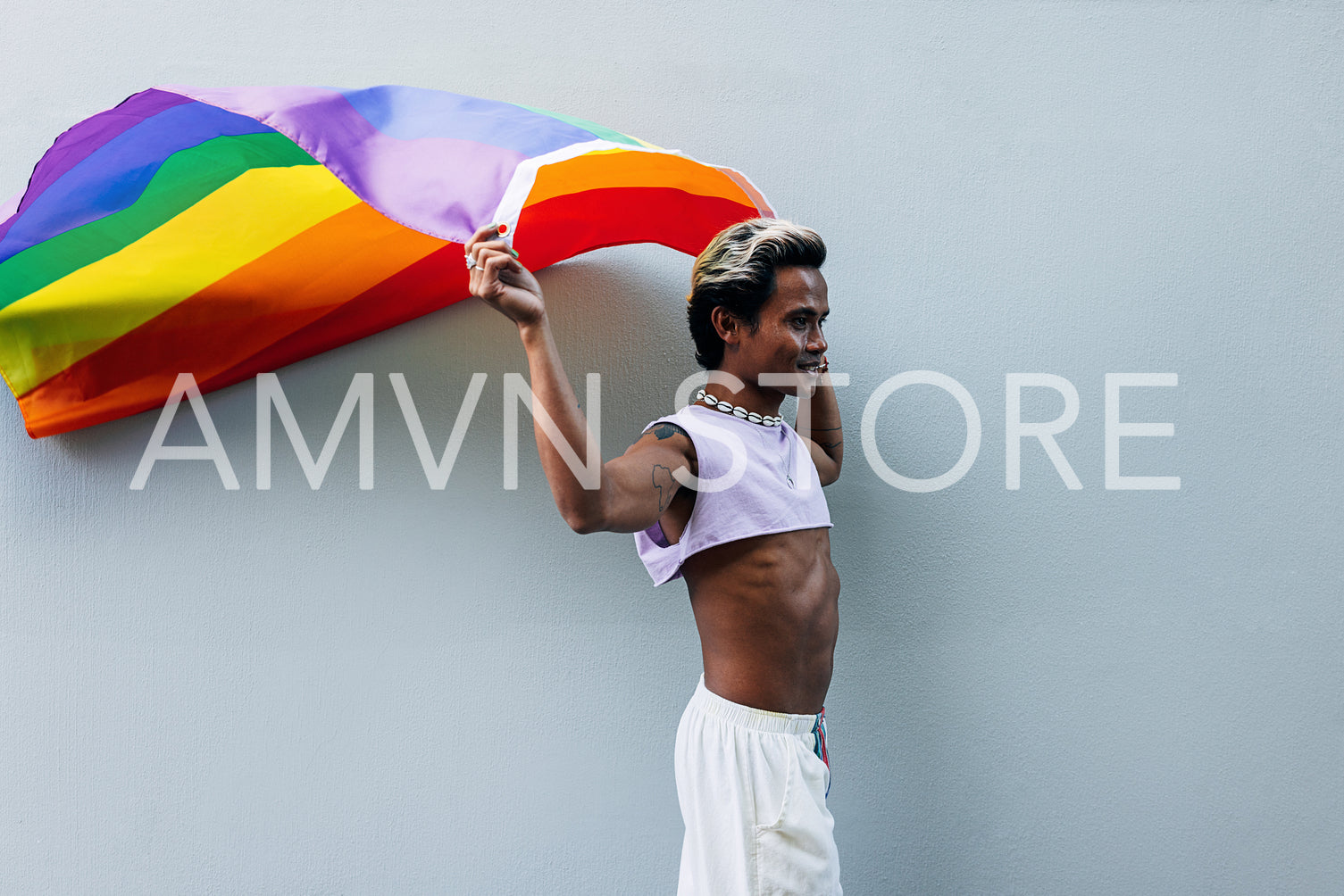 Stylish guy waving LGBT flag while walking at grey wall outdoors