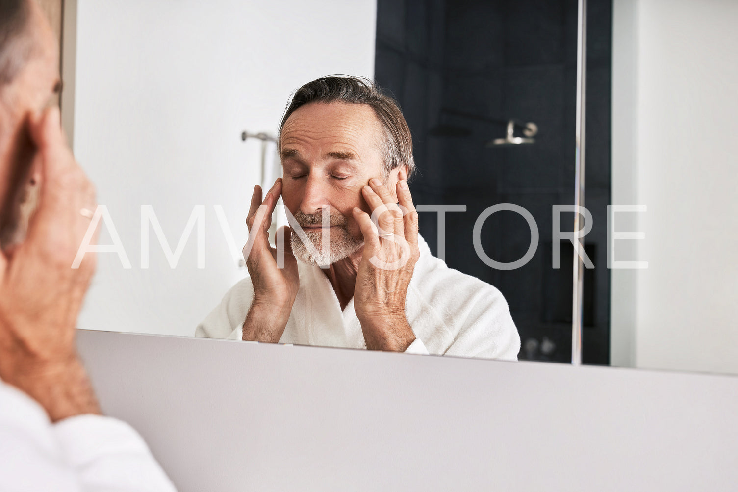 Senior man massaging his face while standing in front of a mirror in bathroom	