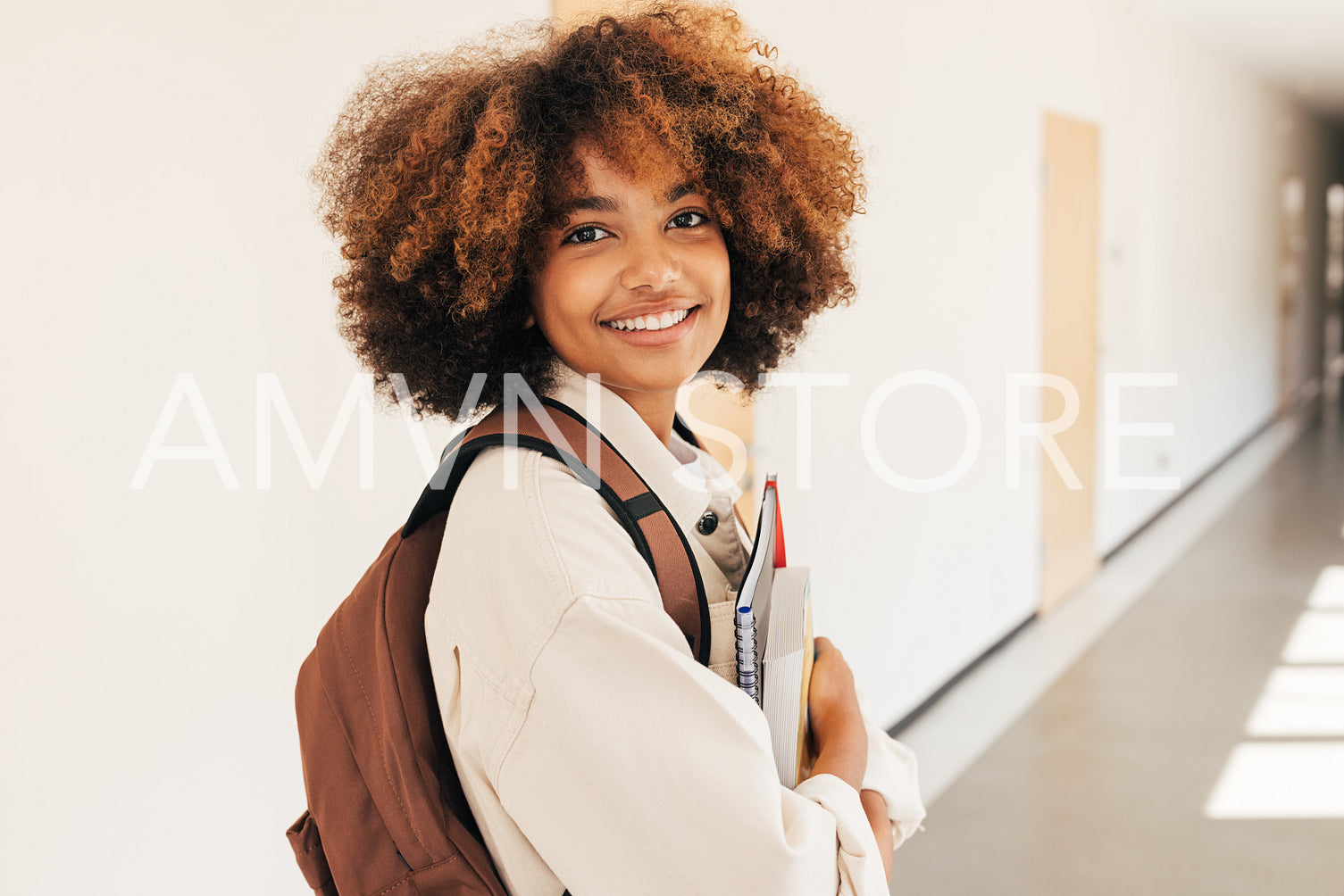 Smiling girl standing in college corridor holding textbooks and looking at camera