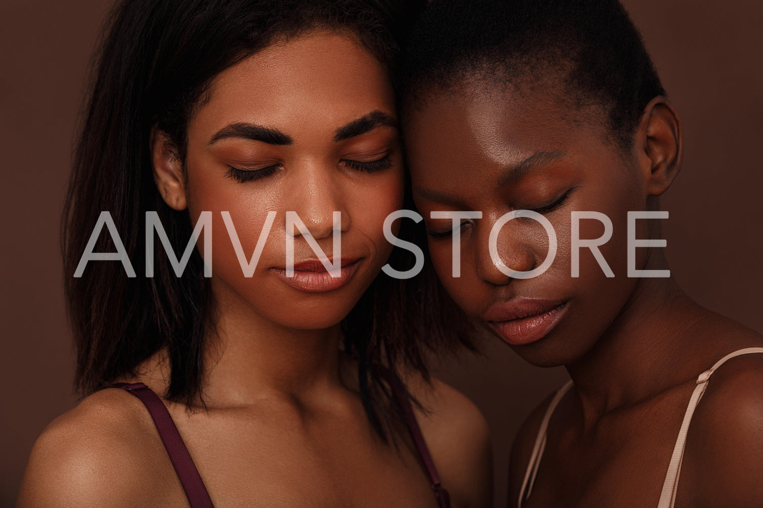 Close up of two beautiful women. Females with closed eyes head to head against a brown backdrop.