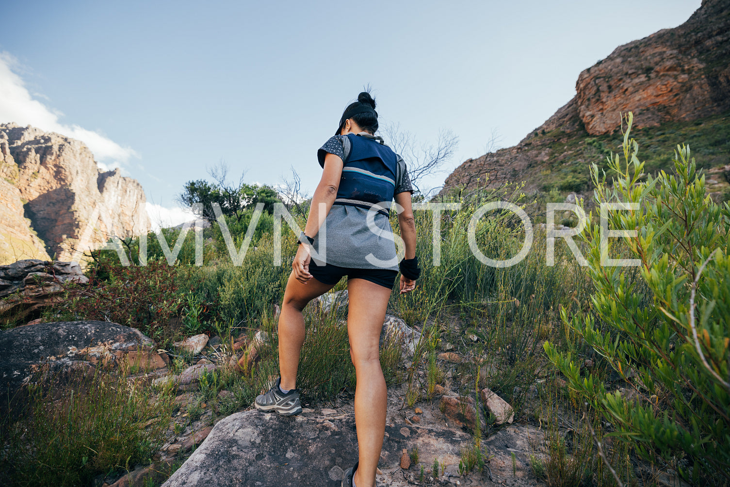 Rear view of woman walking up on mountain trail. Female hiker in sportswear doing hike in wild terrain.