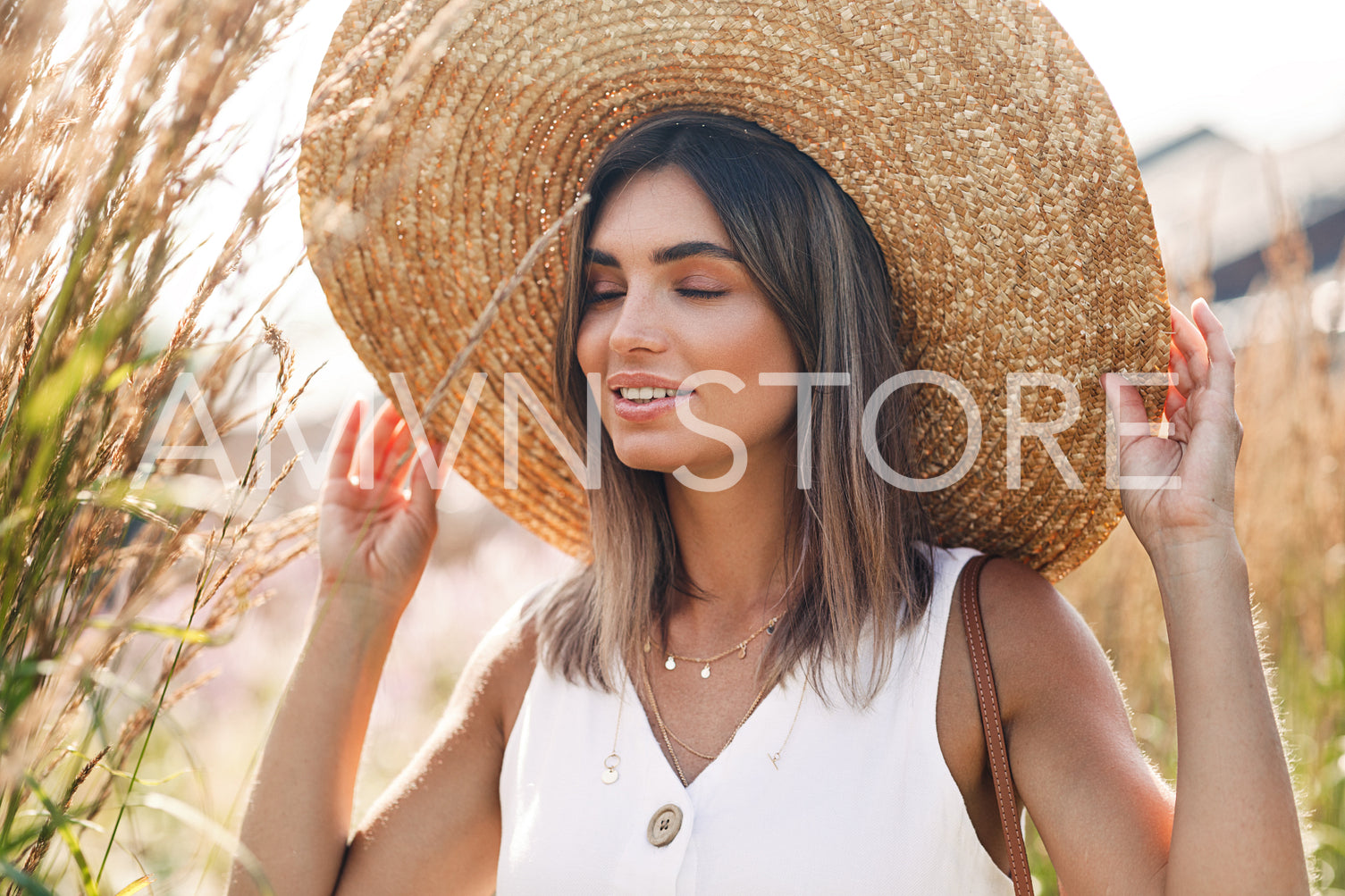 Beautiful blond woman touching her straw hat with eyes closed	