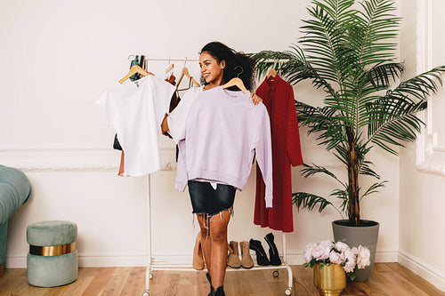 Young personal shopper holding hangers with clothes in studio