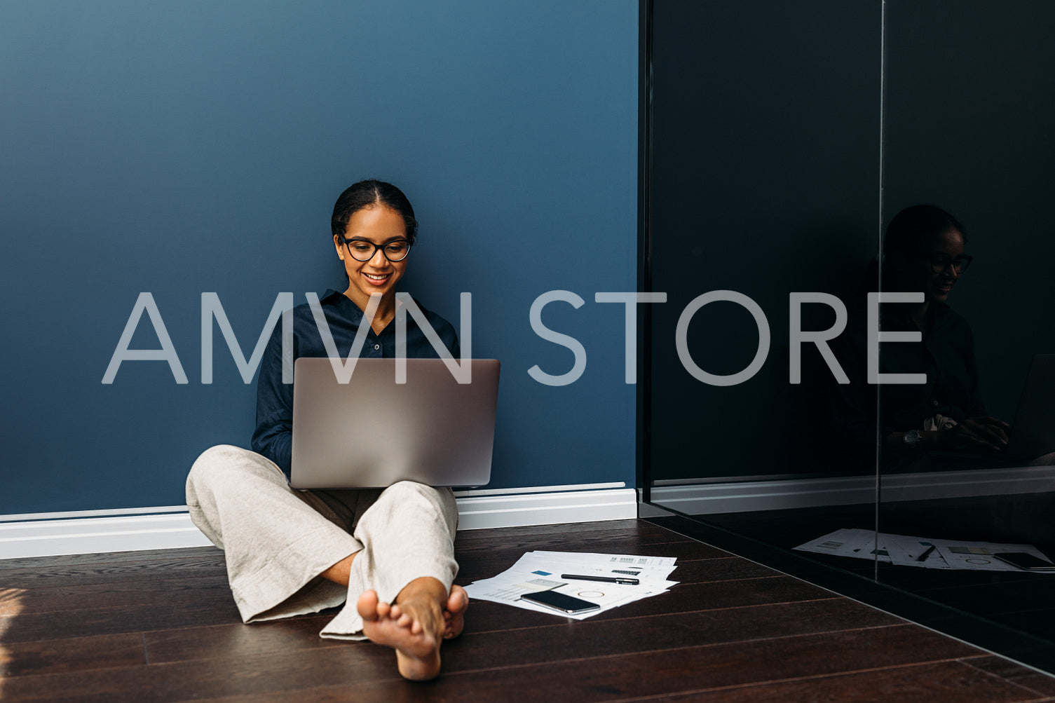 Smiling entrepreneur sitting on the floor at home with a laptop on her legs	